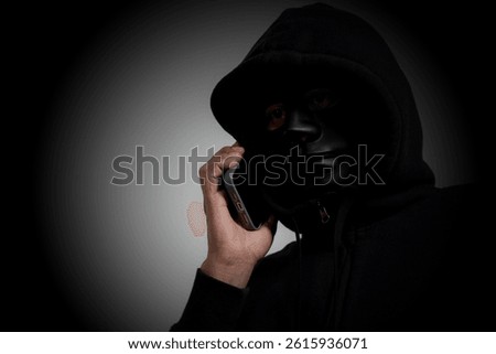 A masked man using a smartphone to deceive others, concept of phone scam and fraud