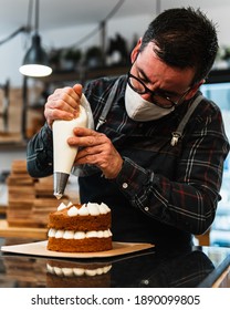 Masked Pastry Chef Filling A Cream Cake With A Piping Bag In A Hipster Bakery