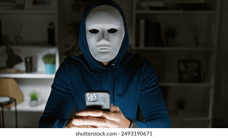 Masked person in hoodie using smartphone indoors, evoking thoughts of privacy, technology, and mystery. - Powered by Shutterstock