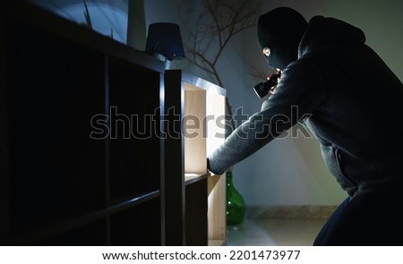 Masked robber with flashlight torch checking apartment.