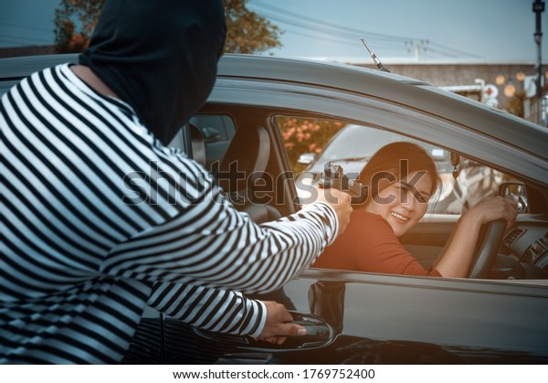 Masked robber with gun threatens a woman and\
forced open the car door.\
Bandit man with masked robber holding\
gun weapon to hijack hostage woman driver in car shocked.\
Thief\
Concept.