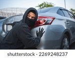 Masked thief in action before burglary. Car thief criminal concept.
