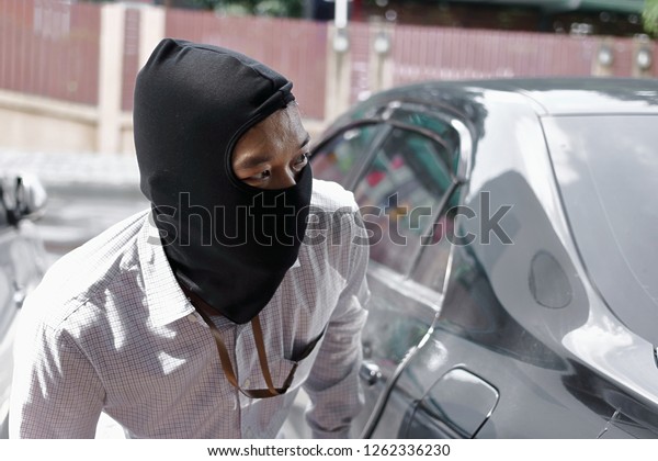 Masked\
thief in black balaclava trying to break into\
car