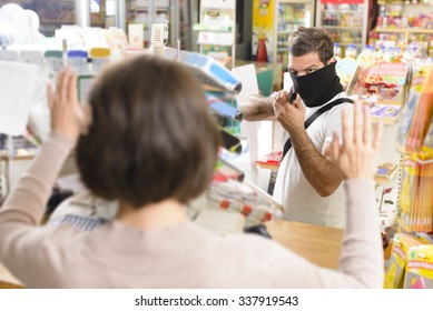 Masked thief pointing a gun to sales woman in a store