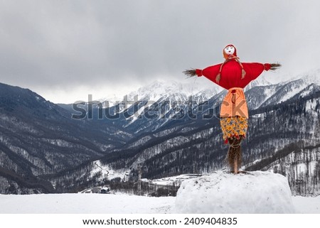 Maslenitsa effigy (a doll made of branches, dressed in a bright skirt, red shirt and scarf) ready for festive burning against the backdrop of the Caucasus mountains. Ski resort Rosa Khutor. Sochi