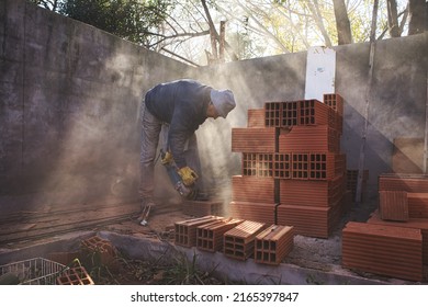 Mason cutting brick with the grinder between sunbeams