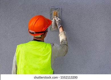 Mason Hand Applying Decorative Plaster On Wall By A Steel Trowel. White Cement Based Decorative Top Coat Plaster Resistant On Outside Whether Conditions. Selective Focus.
