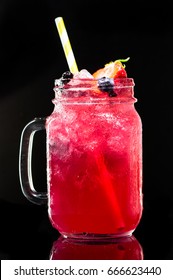 Mason Jar Of Bright Pink Lemonade With Ice, Lemon, Blueberries And Yellow Drinking Straw On Black Background