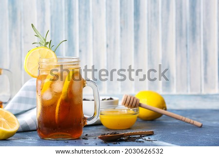 Mason jar of cold black tea with lemon on color background