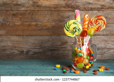 Mason jar with different colorful candies on wooden background. Space for text