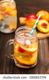 Mason jar glass of homemade peach iced water on a rustic wooden background