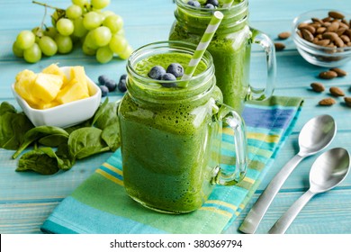 Mason jar mugs filled with green spinach and kale health smoothie with green swirled straw sitting with blue striped napkin and spoons