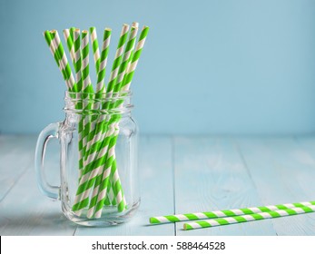 Mason jars with green paper straws on blue wooden background. Ideal for summer drinks and smoothies. Copy space