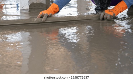 Mason worker working with trowel to level cement floor at construction site. A skilled construction worker spreading wet concrete to level wet concrete on a site floor. Foundation and flooring tasks.
