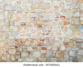 Masonry concept. Old weathered exterior rough strong stonewall background texture. Cobblestone, floor beige brown grey empty for backdrop. Rocks connected with cement solid construction. Border fence.