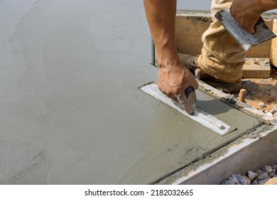 A masonry worker is smoothing the plastering concrete to cement floor while holding steel trowel in his hand