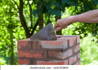 Masonry works,  male hand working with a trowel, repairing a chimney from red bricks on a roof