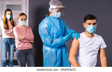 Mass Vaccination Of Staff In The Office. A Nurse In Protective Gear Puts A Prick In A Man's Forearm.