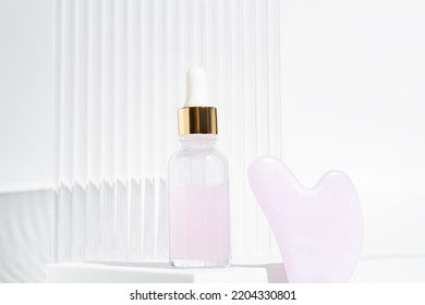 Massage roller for the face made of rose quartz with bottle of cosmetic oil or serum on a white background. The concept of skin care at home