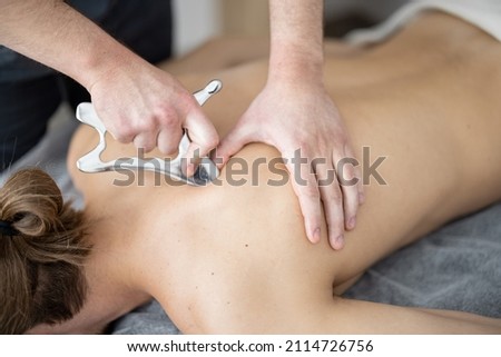 Massage with a special massage blade, kneading trigger points in the shoulders and back, close-up. Therapeutic and relaxing massage after training