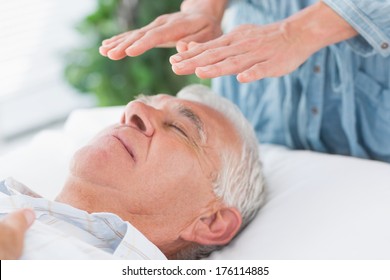 Massage therapist performing Reiki over senior man at health spa - Powered by Shutterstock