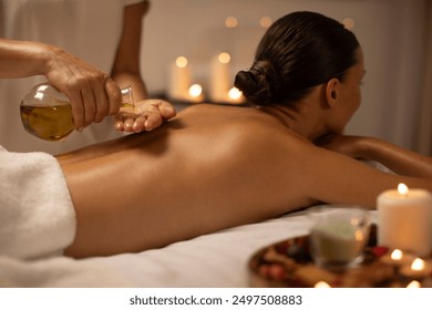 Massage therapist pouring oil on lady back at luxury spa decorated with candles, body care concept. Woman enjoying relaxing massage with aromatherapy - Powered by Shutterstock