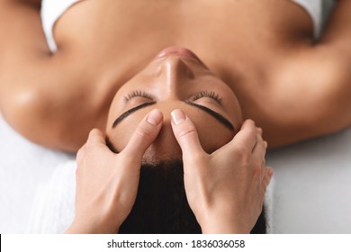 Massage therapist rubbing sleeping black lady forehead, making relaxing head massage, spa salon interior, closeup. Top view of african american young woman getting healing acupuncture procedure