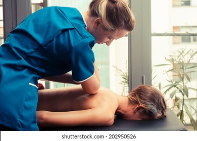 A Massage Therapist Is Treating A Female Client On A Table By The Window