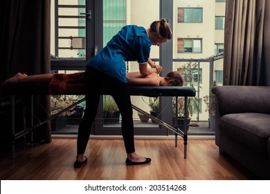 A Massage Therapist Is Treating A Female Client On A Table In An Apartment