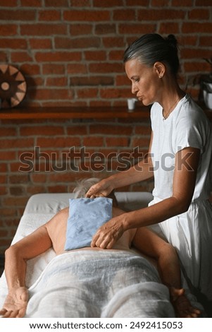 Massage therapist is using a heated pad on the back of a client resting on a massage table