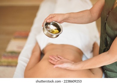 Massage therapist's hands pouring essential oil from bowl on patient's back lying close-up - Shutterstock ID 2238609253