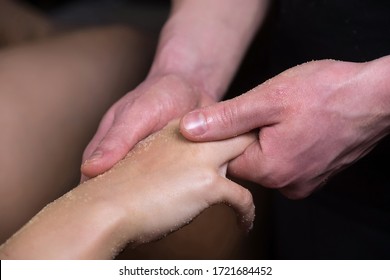 Massagist man scrubbing woman's hand and fingers natural scrub in spa salon. Procedure of peeling and massaging body for young girl in cosmetology clinic, hands closeup. Skincare bodycare concept.