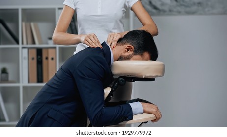 Masseur doing neck massage to businessman in suit in office 