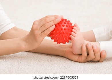 Masseur hand holding red massage ball and massaging infant foot on carpet. Baby healthcare. Closeup. Side view. - Powered by Shutterstock