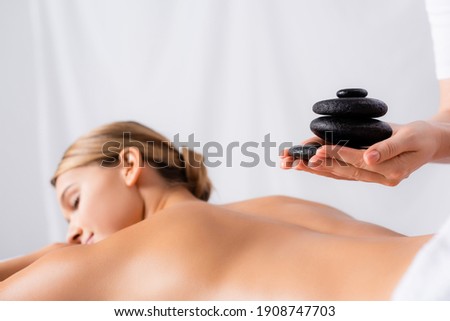 masseur holding hot stones near client on blurred background