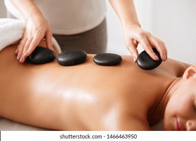 Masseur placing stones on woman's back to perform hot massage, closeup