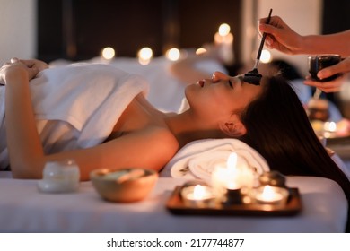 Masseurs Hand Do Holding Glass And Brushing A Facial Mask Herb Black Cream To On Customer's Face As Sleep And Covered Warp By A White On Her Body.