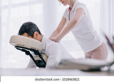 masseuse doing seated back massage for businessman at office