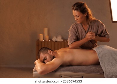 Masseuse gives a man a massage with her elbow in a romantic setting, Relaxing massage in a warm candlelit setting - Powered by Shutterstock