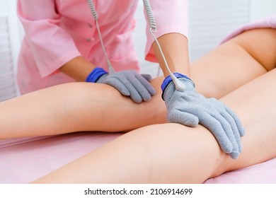 Masseuse makes an anti-cellulite massage on legs. Micro-sensory electric micro-current procedure bio ems for electrode stimulation of the face and body in conductive gloves. Anti-aging lifting