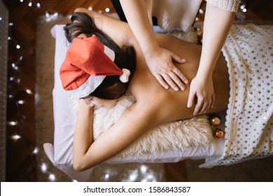 Masseuse massaging girl with Christmas lights in background