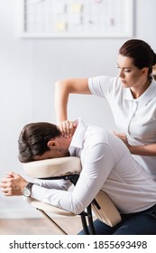 Masseuse Massaging Neck Of Businessman Sitting On Massage Chair In Office On Blurred Background