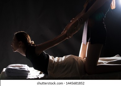 Masseuse stretching bending back massage Asian woman on shoulder neck and spine back in spa room, to release pain relax and stress. Traditional Thai massage Therapy concept, low light dark background
