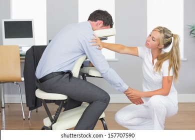 Masseuse treating clients arm in massage chair in bright room