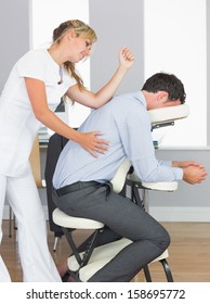 Masseuse treating clients back with elbow in massage chair in bright room