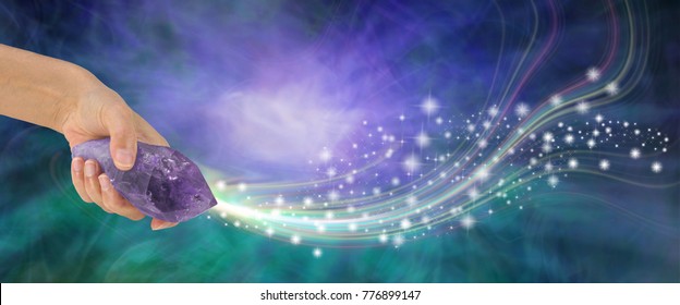 Massive Amethyst with beautiful energy - female hand holding large terminated amethyst quartz wand  shooting out sparkles across a purple and jade energy background with copy space
