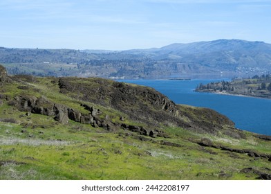 Massive blue river flowing between rolling hills, with a rock-strewn meadow in the foreground on a clear sunny day.  - Powered by Shutterstock