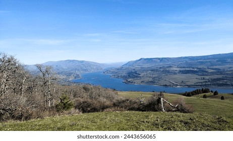 Massive blue river flowing between rolling hills, with a rock-strewn meadow in the foreground on a clear sunny day. - Powered by Shutterstock