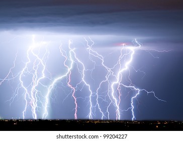 Massive colorful cloud to ground lightning bolts hitting the horizon of city lights.