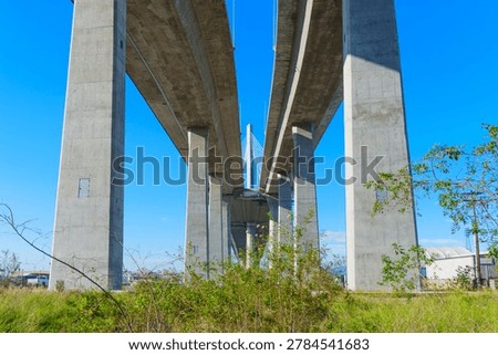 Massive concrete pillars and structural decks of Long Beach International Gateway Bridge viewed from below under clear blue sky. Industrial architecture in Los Angeles port area.